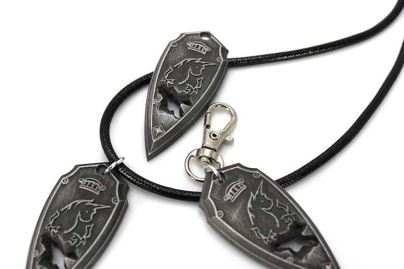 May include: Three silver-toned pendants with a unicorn design, hanging on a black cord. The pendants are shaped like shields with a crown on top.