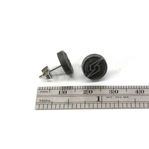 May include: A pair of grey stud earrings featuring a stylised lightning bolt logo. The earrings are approximately 1.5 cm in diameter.