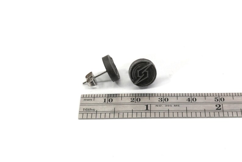 May include: A pair of grey stud earrings featuring a stylised lightning bolt logo. The earrings are approximately 1.5 cm in diameter.