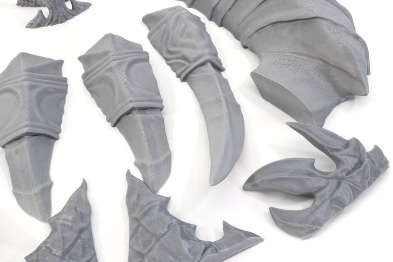 Pode incluir: Um conjunto de pe&ccedil;as de pl&aacute;stico cinzento impressas em 3D para uma figura em miniatura. As pe&ccedil;as incluem um par de bra&ccedil;os, um par de pernas, uma cauda, um par de asas e uma cabe&ccedil;a.