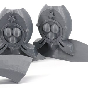 May include: Two gray 3D printed decorative pieces with a star and three circles design. The pieces are on a white surface.