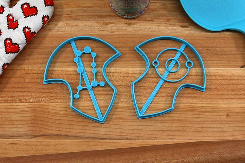 Puede incluir: Dos cortadores de galletas de pl&aacute;stico azul, uno con forma de constelaci&oacute;n y el otro con forma de nave espacial.
