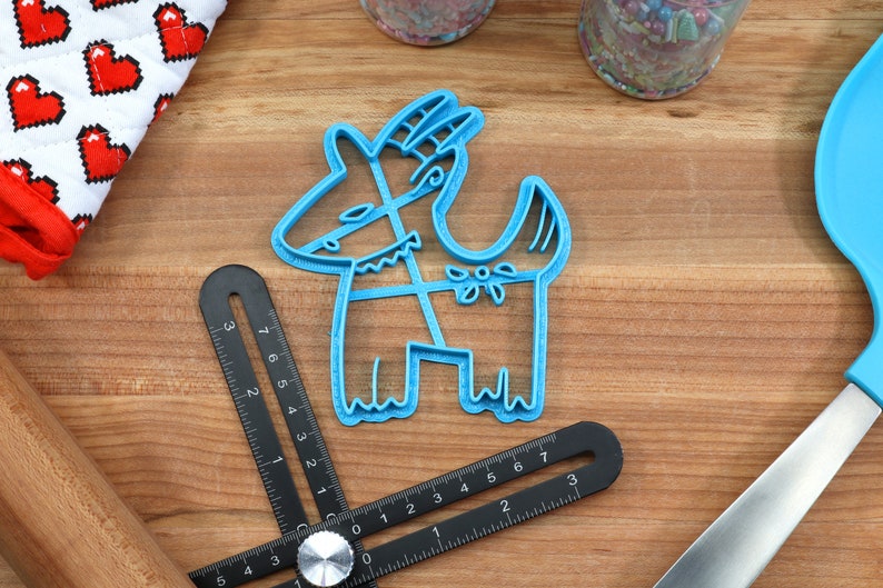 Puede incluir: Un cortador de galletas de pl&aacute;stico azul con forma de cabra estilizada con detalles florales.