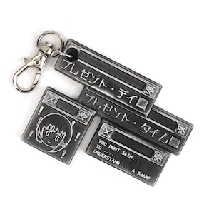 May include: A silver metal keychain with four charms. The charms are shaped like computer windows with the text "プレゼント・タイム" (present-time) in Japanese. The bottom charm has the text "YOU DONT SEEM... TO UNDERSTAND... A SHAME".