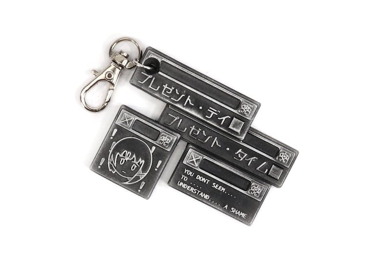 May include: A silver metal keychain with four charms. The charms are shaped like computer windows with the text "プレゼント・タイム" (present-time) in Japanese. The bottom charm has the text "YOU DONT SEEM... TO UNDERSTAND... A SHAME".