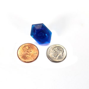 May include: A blue plastic gem-shaped object, about the size of a US penny, is shown next to two US coins: a penny and a dime.