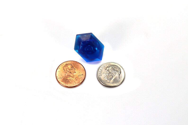 May include: A blue plastic gem-shaped object, about the size of a US penny, is shown next to two US coins: a penny and a dime.