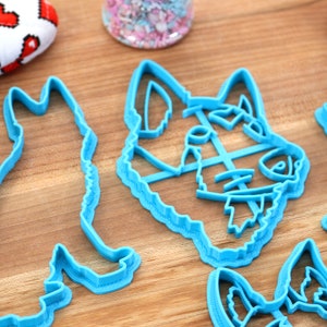 May include: Four blue plastic cookie cutters shaped like dogs. The cutters are on a wooden surface.