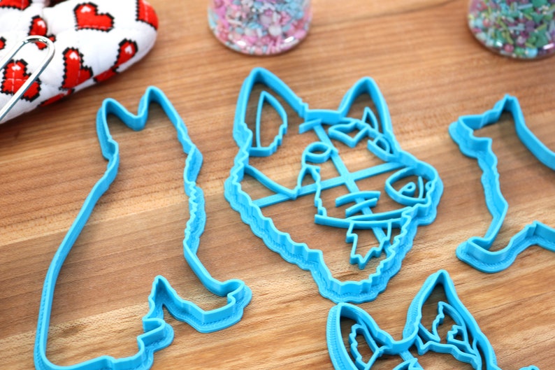 May include: Four blue plastic cookie cutters shaped like dogs. The cutters are on a wooden surface.