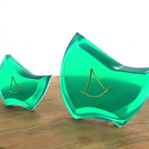 May include: Two green glass paperweights with a gold sailboat design. The paperweights are on a wooden surface.