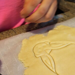 May include: A close-up of a cookie dough cutout in the shape of a bird on a white baking sheet lined with parchment paper.