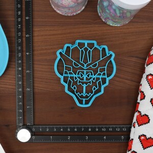 May include: A blue plastic cookie cutter shaped like a dragon's head. The cutter is on a wooden surface.