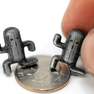 May include: Two small, gray, 3D printed figurines of a character from a video game. The figurines are standing on a US dime.