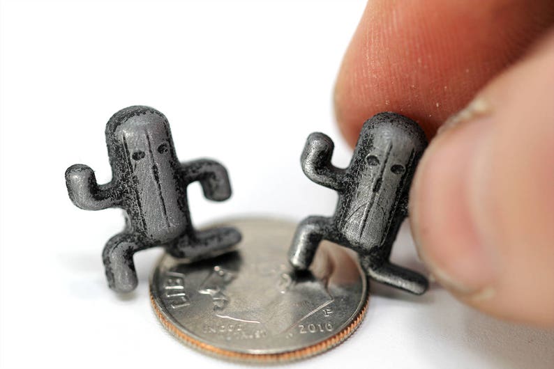 May include: Two small, gray, 3D printed figurines of a character from a video game. The figurines are standing on a US dime.