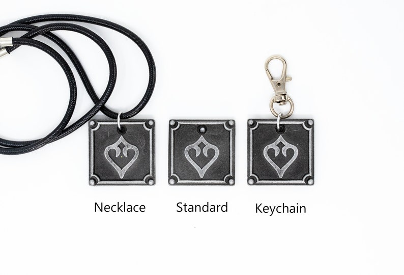 May include: Three versions of a silver-colored pendant with a stylized heart design. The pendant is available as a necklace, keychain, or standard pendant.