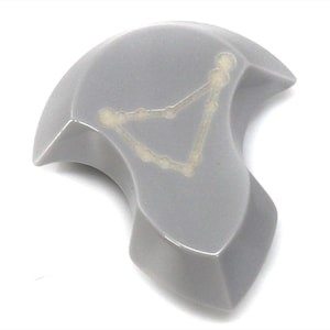 Op de afbeelding: Een grijs keramisch gerecht in de vorm van een halve maan met een witte omtrek van het sterrenbeeld Steenbok.