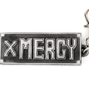 May include: A silver keychain with a black rectangular tag that says "X MERCY" in a pixelated font.