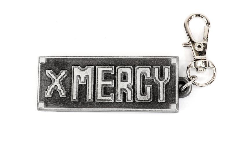 May include: A silver keychain with a black rectangular tag that says "X MERCY" in a pixelated font.