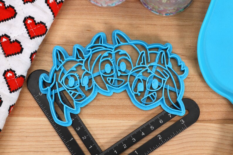 May include: Blue plastic cookie cutter shaped like three cartoon characters with big eyes and smiles. The characters are side by side and appear to be friends.