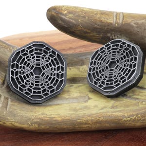 May include: Two silver-colored octagonal earrings with a geometric design. The earrings have a raised, intricate pattern that resembles a honeycomb or a web.