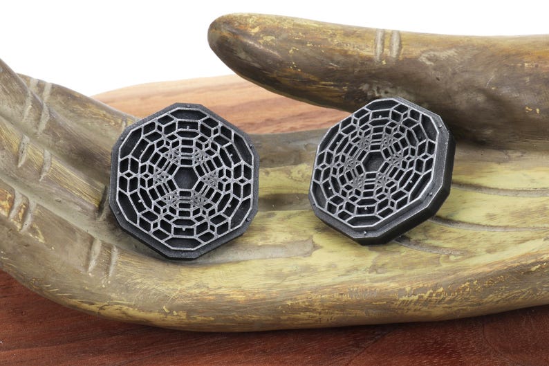 May include: Two silver-colored octagonal earrings with a geometric design. The earrings have a raised, intricate pattern that resembles a honeycomb or a web.