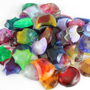 May include: A collection of colorful, translucent, resin game pieces in various shapes, including stars and crescent moons. Each piece features a unique design and intricate details.