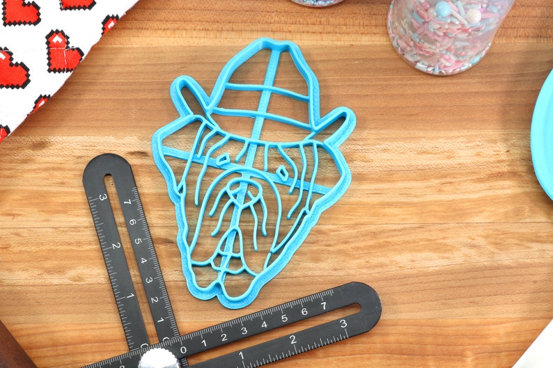 Peut inclure: Un emporte-pi&egrave;ce en plastique bleu en forme de bouledogue portant un chapeau. L'emporte-pi&egrave;ce est sur une surface en bois.