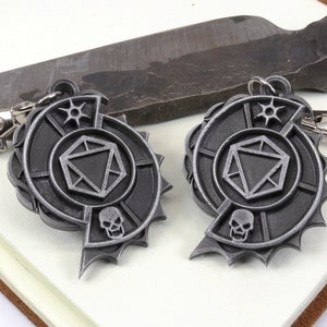 May include: Two silver metal keychains with a skull and a die design. The keychains are in the shape of a spiral with a star at the top.