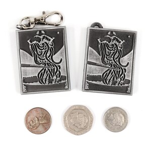 May include: Two silver keychains with a black and white image of a creature with tentacles. The keychains are on a white background with three coins.