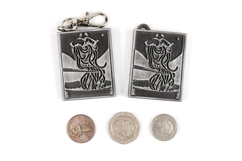 May include: Two silver keychains with a black and white image of a creature with tentacles. The keychains are on a white background with three coins.