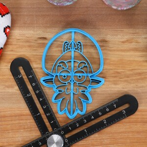 May include: Blue plastic cookie cutter shaped like a cartoon character with a beard and a hat. The character has large eyes and a wide smile.