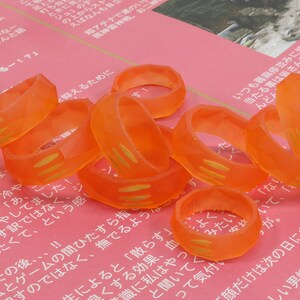 May include: A group of orange plastic rings with gold accents. The rings are stacked on top of each other and are arranged in a circular pattern.