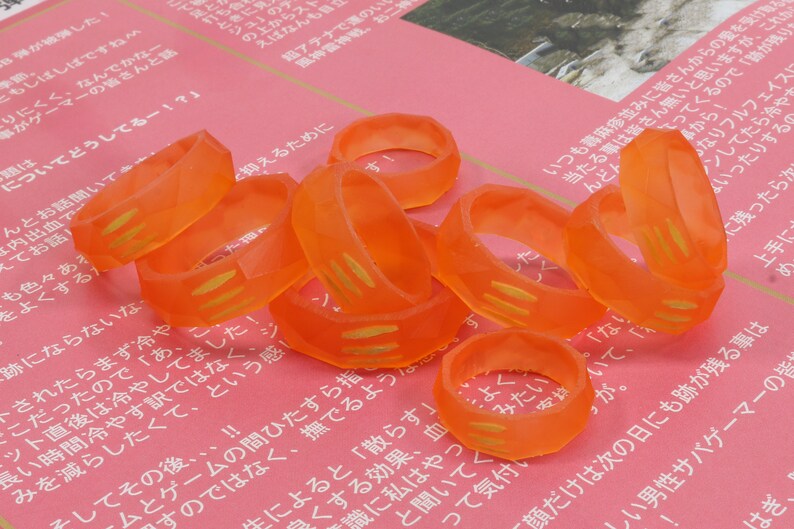 May include: A group of orange plastic rings with gold accents. The rings are stacked on top of each other and are arranged in a circular pattern.