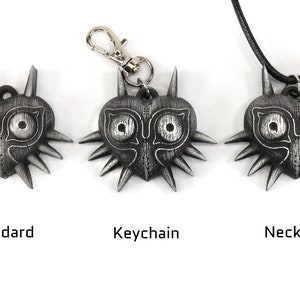 May include: Three versions of a Majora's Mask pendant: a standard pendant, a keychain, and a necklace. Each pendant is a silver-colored heart-shaped mask with a stylized face and spikes.