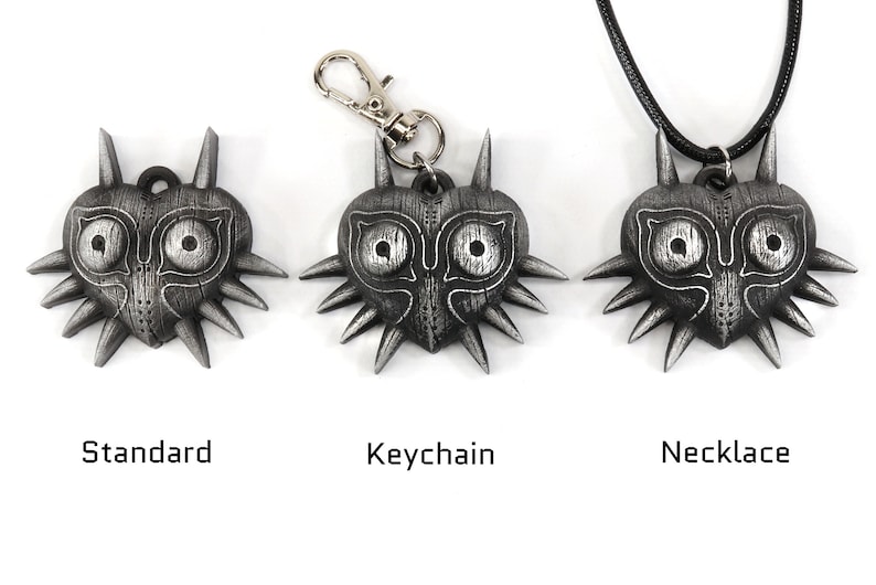 May include: Three versions of a Majora's Mask pendant: a standard pendant, a keychain, and a necklace. Each pendant is a silver-colored heart-shaped mask with a stylized face and spikes.