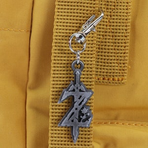 May include: A silver metal keychain charm shaped like a sword with a stylized letter Z on a yellow backpack.