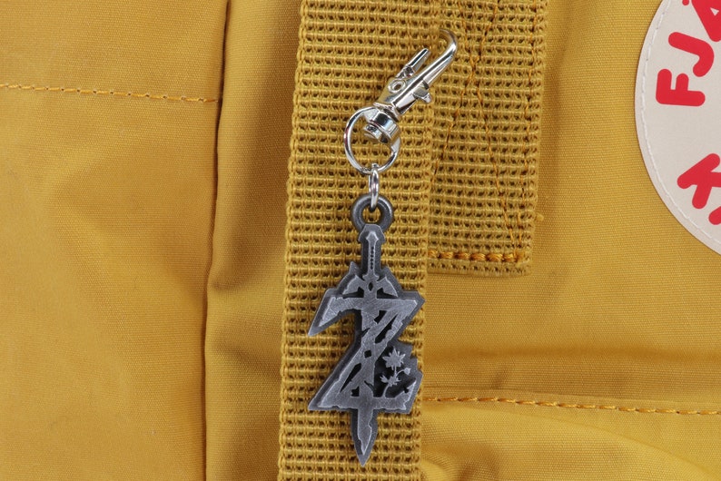 May include: A silver metal keychain charm shaped like a sword with a stylized letter Z on a yellow backpack.