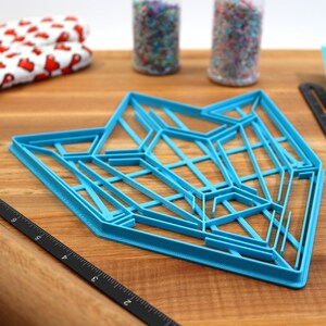 Puede incluir: Un cortador de galletas geom&eacute;trico de pl&aacute;stico azul sobre una superficie de madera. El cortador tiene forma de estrella con m&uacute;ltiples puntos y l&iacute;neas.