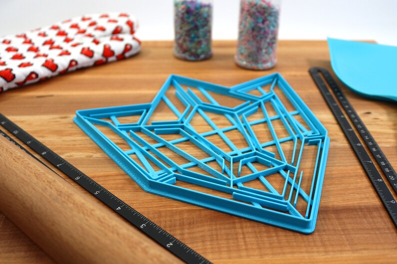 Puede incluir: Un cortador de galletas geom&eacute;trico de pl&aacute;stico azul sobre una superficie de madera. El cortador tiene forma de estrella con m&uacute;ltiples puntos y l&iacute;neas.
