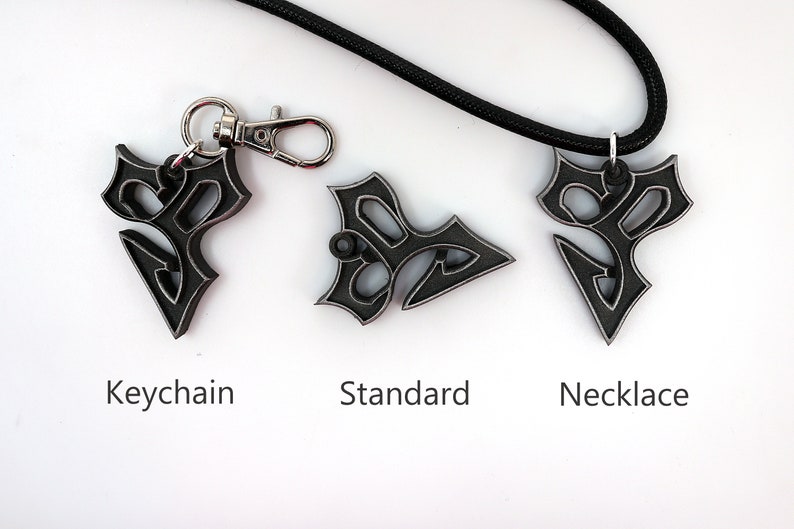 May include: Three versions of a black metal pendant with a stylized design. The pendant is shown as a keychain, a standard pendant, and a necklace.