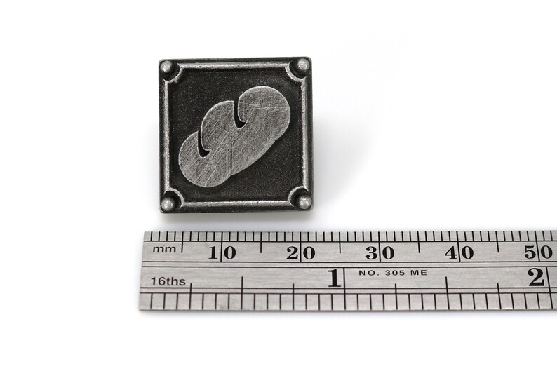 May include: A silver-colored metal pin with a black background. The pin features a stylized image of a loaf of bread. The pin is approximately 2 cm wide.