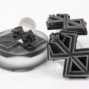 May include: Three black geometric snowflake-shaped ear gauges. The gauges are made of a smooth, matte material and have a detailed design.