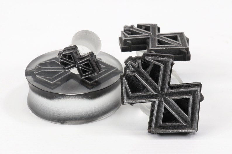 May include: Three black geometric snowflake-shaped ear gauges. The gauges are made of a smooth, matte material and have a detailed design.