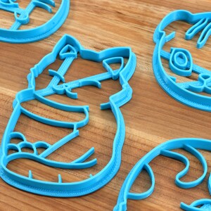 May include: A set of five blue plastic cookie cutters shaped like animals. The cutters are on a wooden surface.