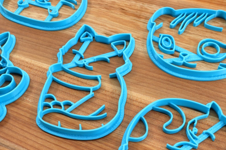 May include: A set of five blue plastic cookie cutters shaped like animals. The cutters are on a wooden surface.