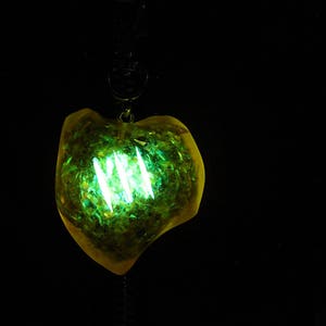 May include: A yellow heart-shaped pendant with green glitter and a glowing green light inside.