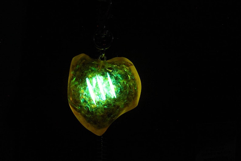 May include: A yellow heart-shaped pendant with green glitter and a glowing green light inside.