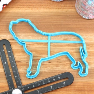 Peut inclure: Un emporte-pi&egrave;ce en plastique bleu en forme de chien. L'emporte-pi&egrave;ce est sur une surface en bois avec une r&egrave;gle &agrave; c&ocirc;t&eacute;.