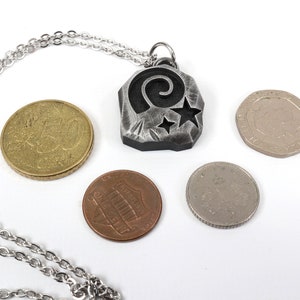 May include: A silver necklace with a pendant featuring a stylized spiral and stars. The pendant is about the size of a US quarter.