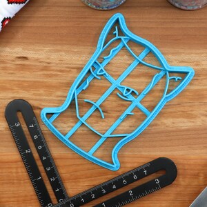 May include: A blue plastic cookie cutter shaped like a dog's head. The cutter has a detailed design with lines and curves.